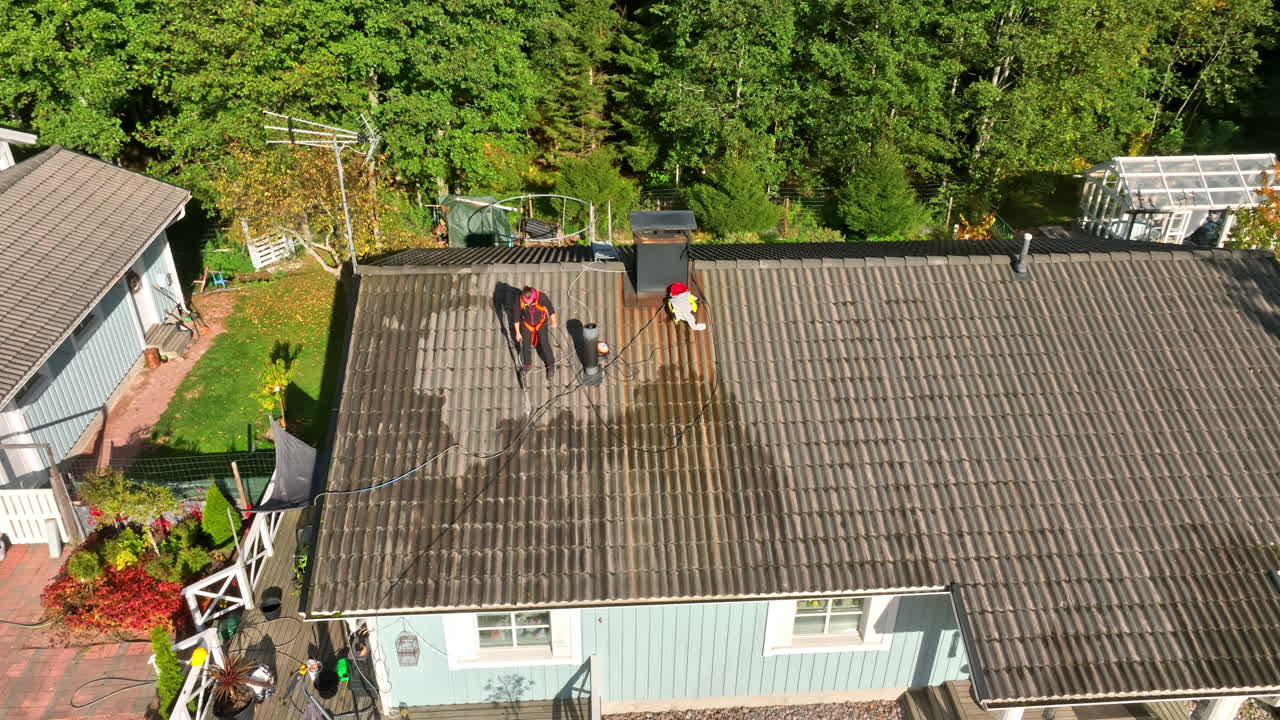 Aerial view around a woman washing a house roof, sunny, autumn day in Finland