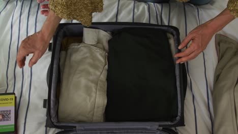 hands of caucasian senior couple packing covid vaccinate passport into suitcase