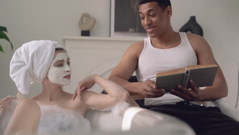 woman with face mask taking a relaxing bath, black man reads a book