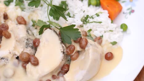 vista ravvicinata del riso con besciamella e uvetta insieme alla carne bollita con carote e piselli e coriandolo in cima in un piatto bianco su un tavolo di legno