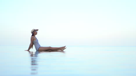 A-sexy-young-woman-sits-on-the-edge-of-an-infinity-pool,-giving-the-illusion-that-she-is-floating-in-midair