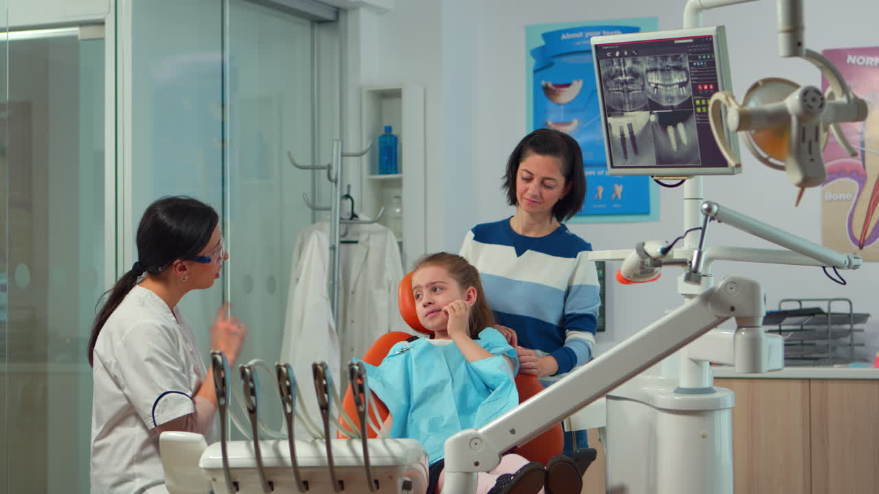 Pediatric woman dentist talking with mother and girl about oral hygiene