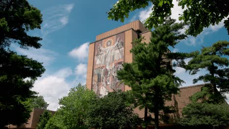 Hesburgh-Library-with-World-of-Life-mural,-Touchdown-Jesus-on-the-campus-of-Notre-Dame-University-of-South-Bend,-Indiana-with-state-wide-shot-view-through-trees-shot