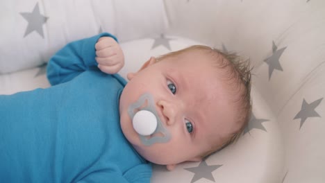 lovely little boy sucks dummy resting in soft cocoon in crib