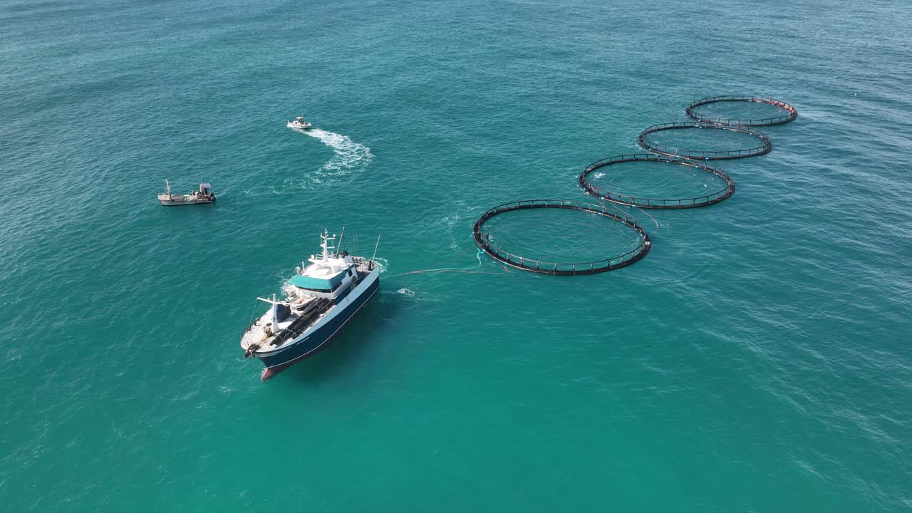 A Mid sized marine vessel tows four fish farms along the west Australian coast.