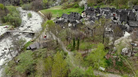 aerial flyover over the village of foroglio in ticino, switzerland with a pan up camera motion from the rooftops up to the big waterfall