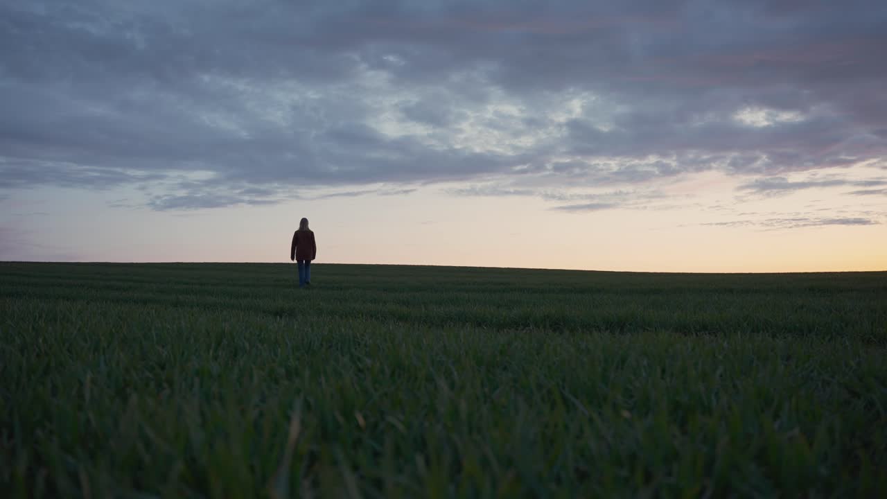 Girl walking up a grass hill at sunset