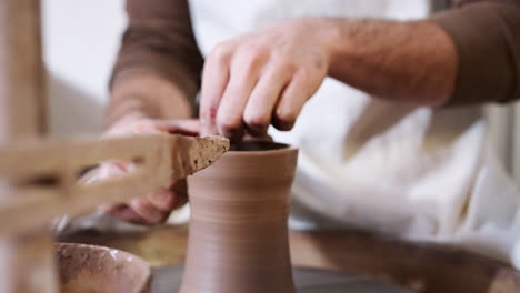 close up of hands of man wearing apron working at pottery wheel making vase in ceramics studio