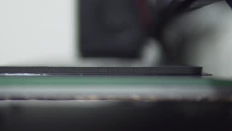 super close up with a shallow depth of field to a 3d printer extruder while working, with black pla filament and glass heated bed