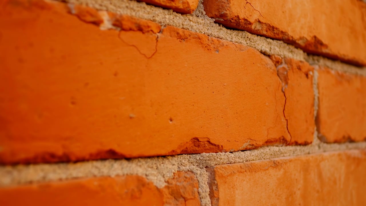 Close-up of an orange brick wall filling the frame, showing rough mortar joints, weathered surfaces, and shallow focus. The main subject sits slightly right