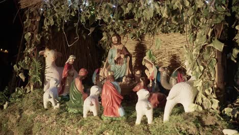 hand painted nativity figurines arranged in moss-filled stable with leafy backdrop