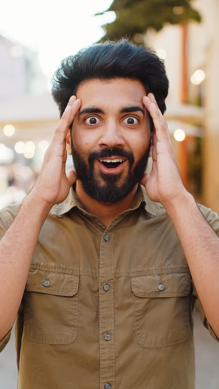 Young man looking surprised at camera shocked by sudden win good victory news wow in city street