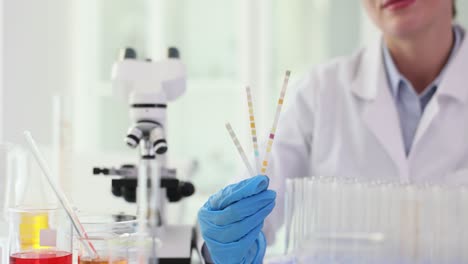 scientist in a lab coat holding test strips with a microscope in the background