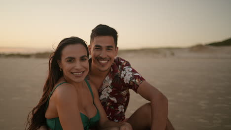 pareja feliz sentada en la arena y posando