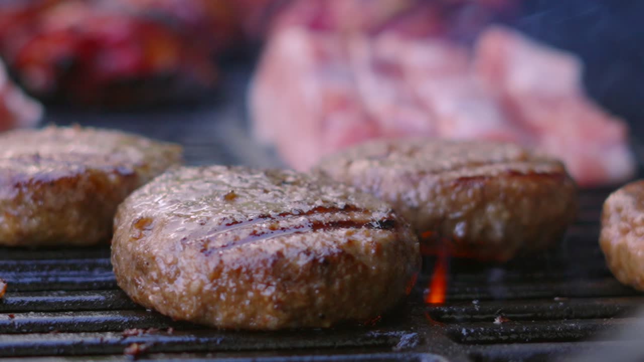 Slow Motion Flames Gently Rising and Cooking Delicious BBQ Beef Burgers on Iron Grill. Close Up Slow Motion Barbecue Summer Cooking Food.