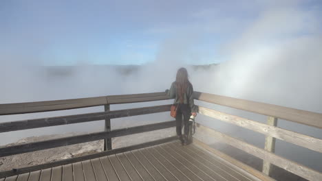 Young-Female-Photographer-on-Lookout-Above-Dense-Steam-in-Yellowstone-National-Park,-Wyoming-USA