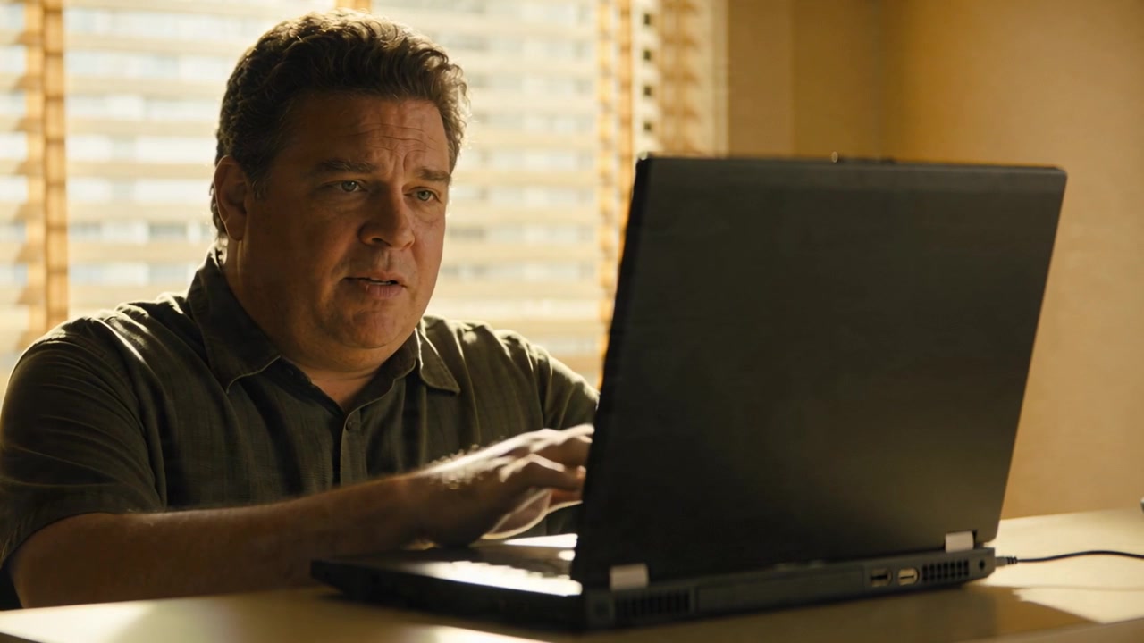 Sonnenblendung bemerkend, Mann im dunklen Hemd stellt den Laptop-Deckel am Tisch ein, tippt, blickt auf, reagiert.
