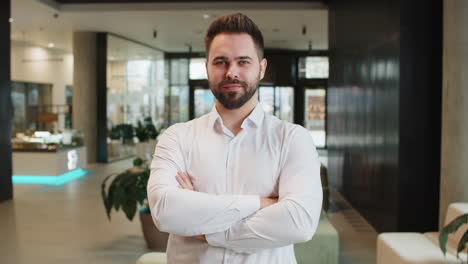 portrait of happy young businessman with arms crossed looking at camera in modern office hotel lobby