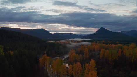 Camera-Follows-River-in-a-Foggy-Morning,-Soaring-Over-Colorful-Trees-with-Shredding-Leaves-in-Washington-Mountainscape