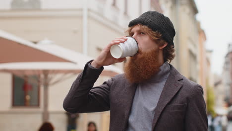 a man with a red beard drinks coffee on a city street