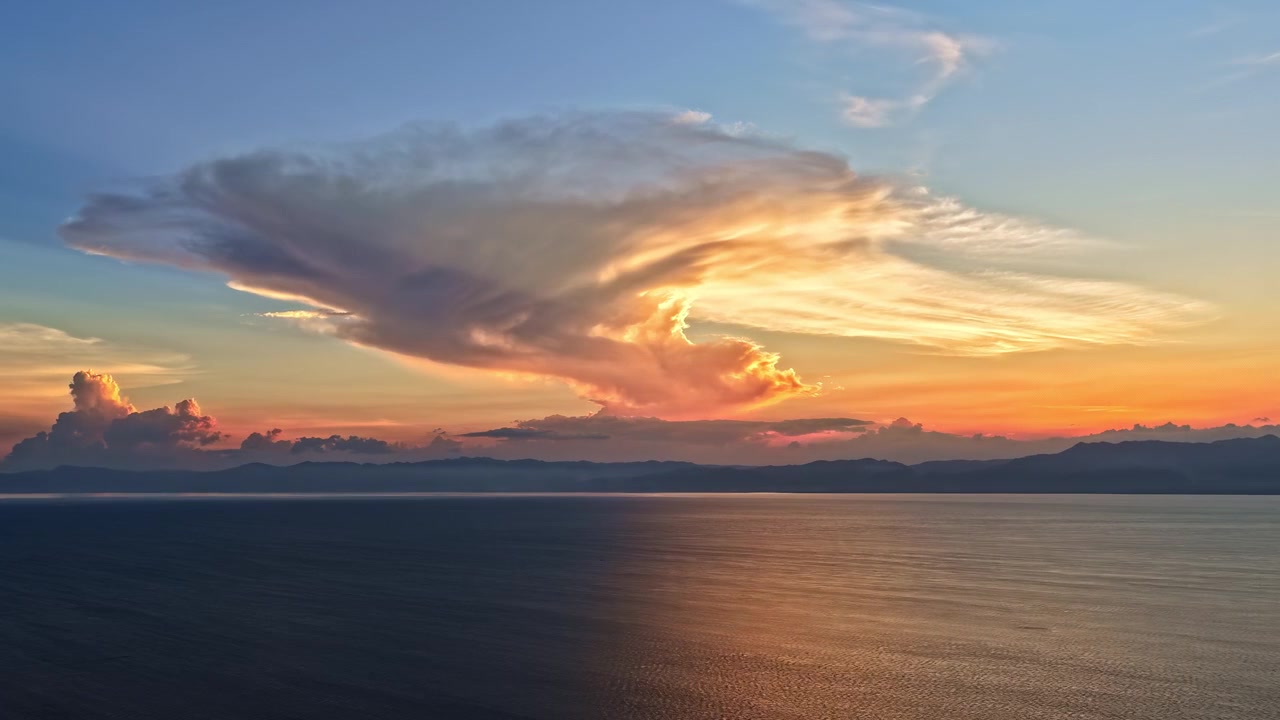 Sunset timelapse with clouds creating vibrant colors over water and distant horizon, aerial view