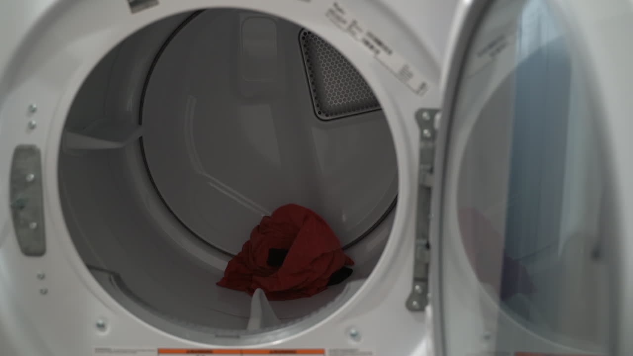 Close up of a man loading clothes into a dryer from the washing machine next to it 