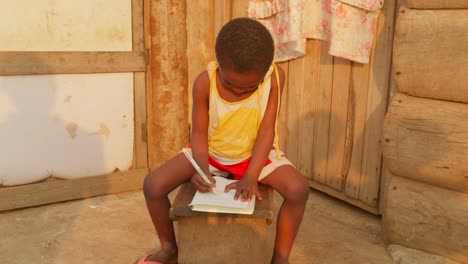 black african children studying alone doing her homework in remote village of africa kid writing and drawing on notebook with pen