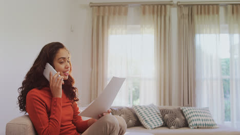 Frau-Sitzt-Auf-Dem-Sofa-Und-Liest-Dokumente,-Während-Sie-Mit-Dem-Mobiltelefon-4k-4k-Spricht