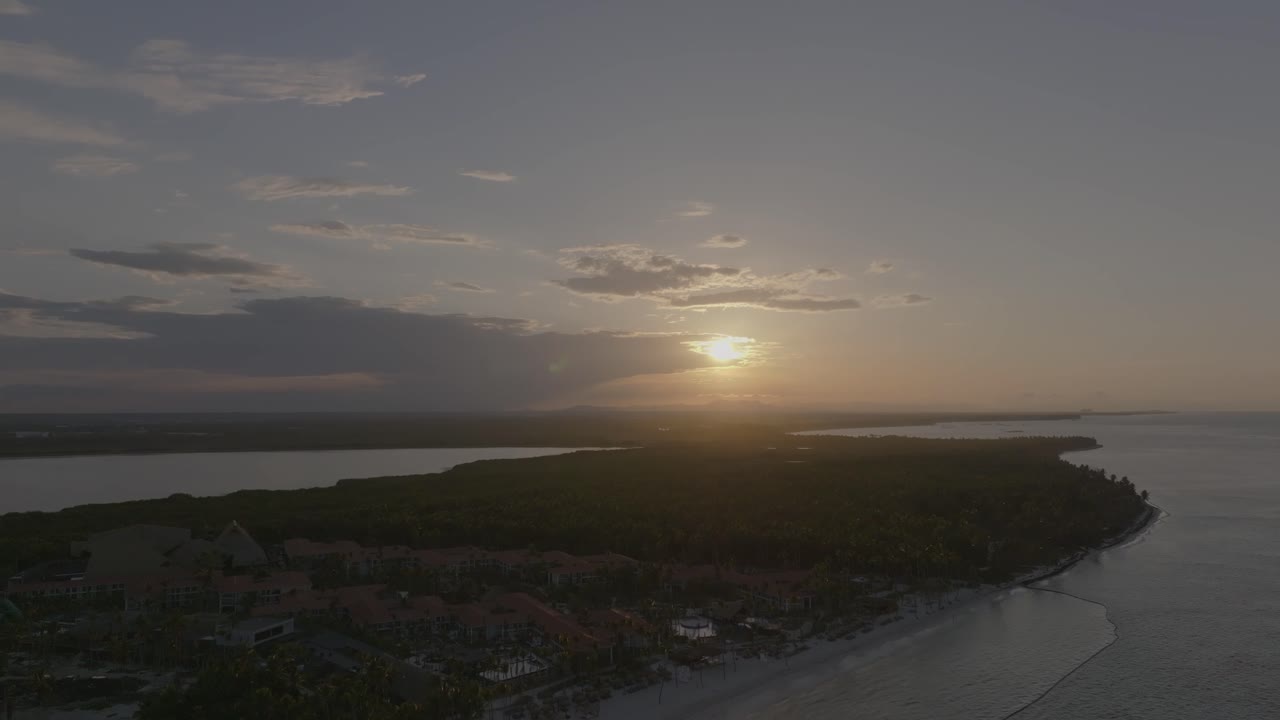 Evening aerial trucking pan of Cabeza de Toro beach in Punta Cana with waves and golden sun peaking from behind thick clouds
