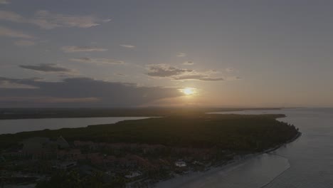 evening aerial trucking pan of cabeza de toro beach in punta cana with waves and golden sun peaking from behind thick clouds