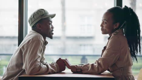 Couple,-laughing-and-holding-hands-on-table