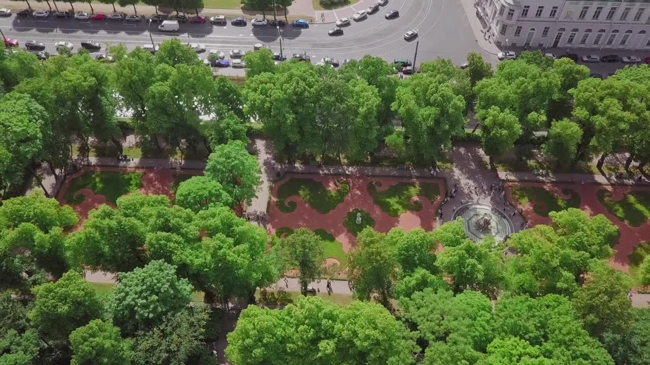 jardín de verano, un dron aéreo pasa volando por una hermosa fuente koronniy desde arriba, gente visitando el festival, con flores y sensación de verano