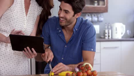 Cute-couple-looking-at-tablet-and-slicing-vegetables