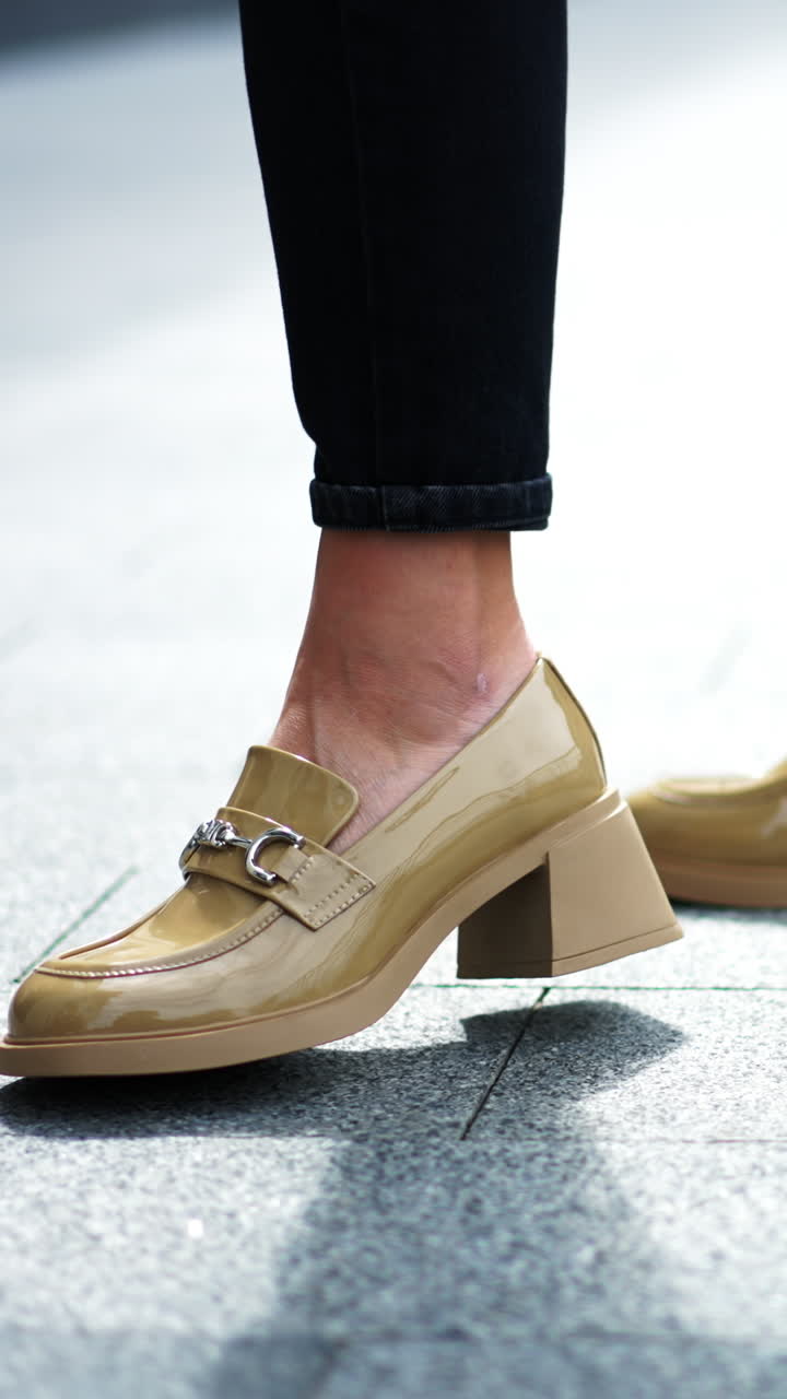 Beige patent leather shoes with metal decoration. Female model in black pants demonstrating the footwear. Close up. Vertical video
