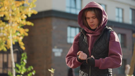 outdoor coach wearing hoodie and black gloves rolls hands gently in urban setting with sunlight highlighting movement and texture as part of warm up training routine for preparation and calm focus