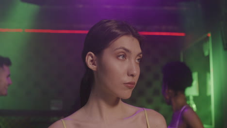 portrait of beautiful girl looking confident at camera at disco while her friends dancing behind her 1 1