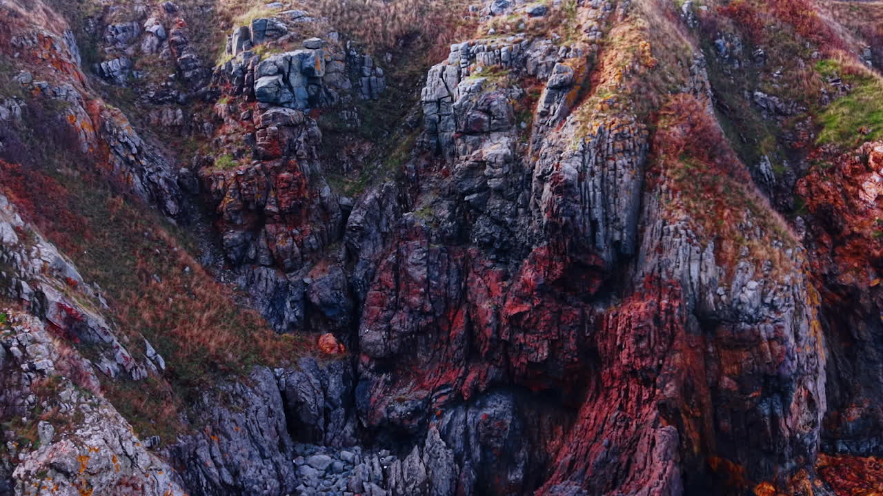 Scogliere a picco sul mare con pietre grezze e chiazze di muschio verde. Le rocce mostrano diversi colori, a testimonianza della bellezza naturale del paesaggio costiero.