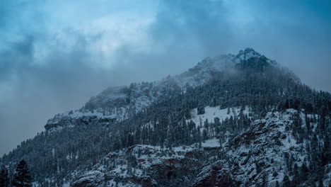 time lapse of cold winter landscape in mountains, dark clouds moving above snow capped hills and forest