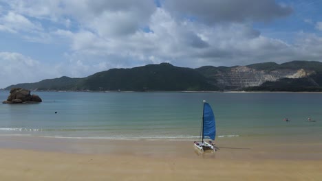 Sailboat-on-Sandy-Beach-Shore-of-Sanya,-China-in-Summer---Aerial-Flight