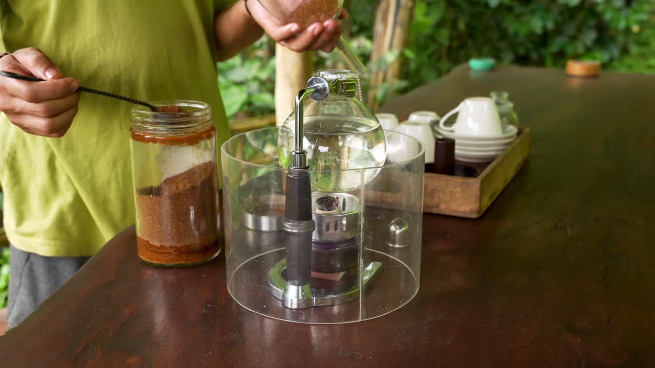 Primo piano di una persona che prepara il caffè con un estrattore a sifone Kopi Luwak in un ambiente naturale all'aperto