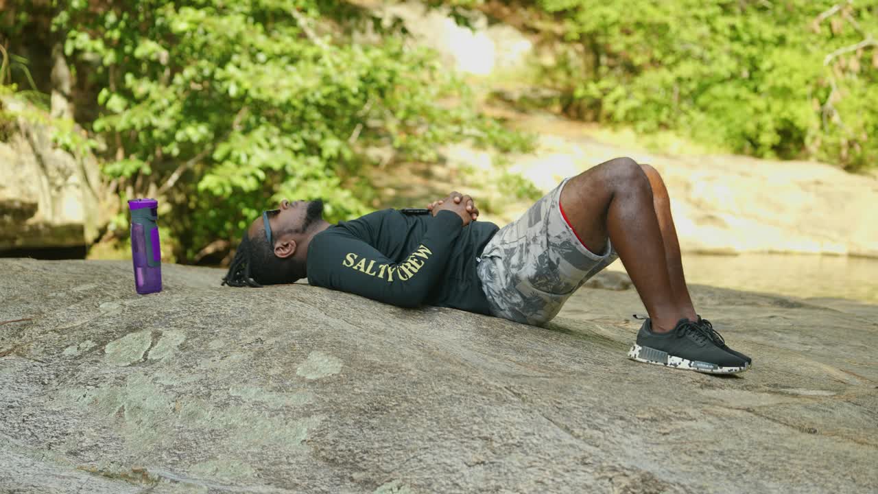 한 남자가 밝고 화창한 날 숲 한가운데 있는 거대한 바위에 누워 휴식을 취합니다