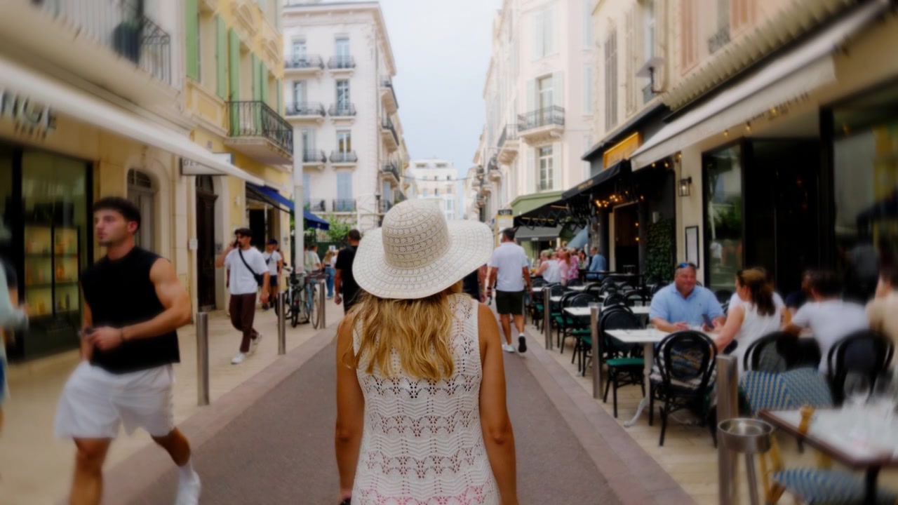 Mulher de chapéu de verão caminha por uma rua de pedestres movimentada com cafés em Cannes, França
