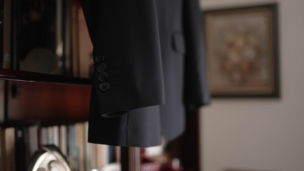 close up of black suit jacket sleeve hanging in home with books in background