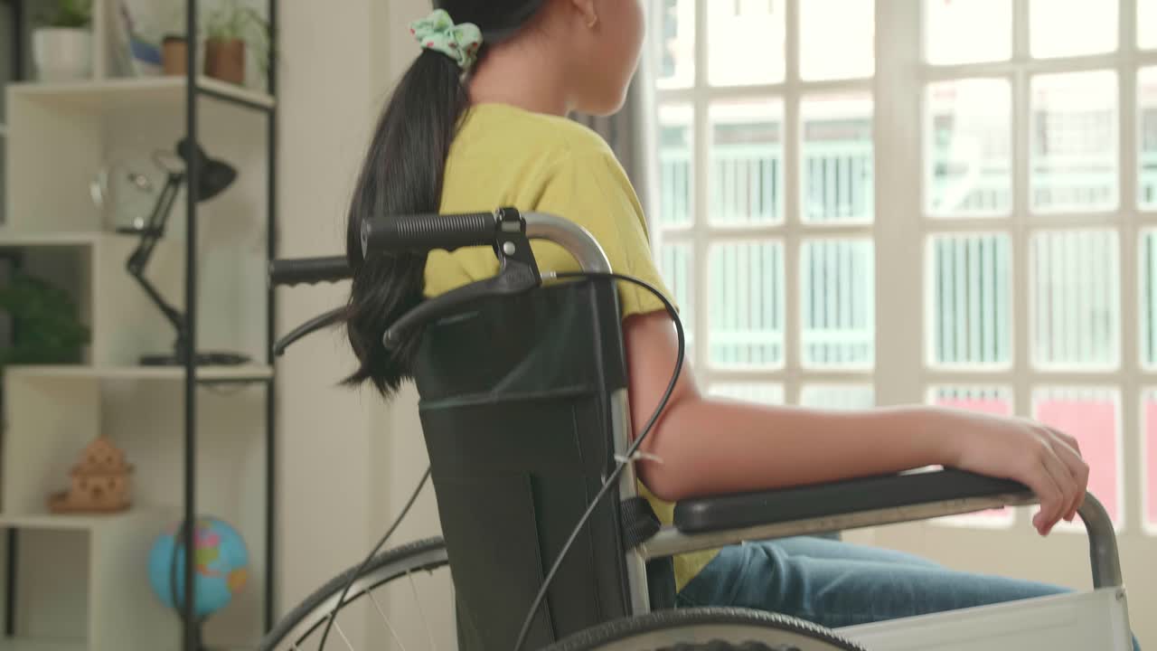 Asian Kid Girl Sitting In A Wheelchair Smiling And Looking At Camera Near Door