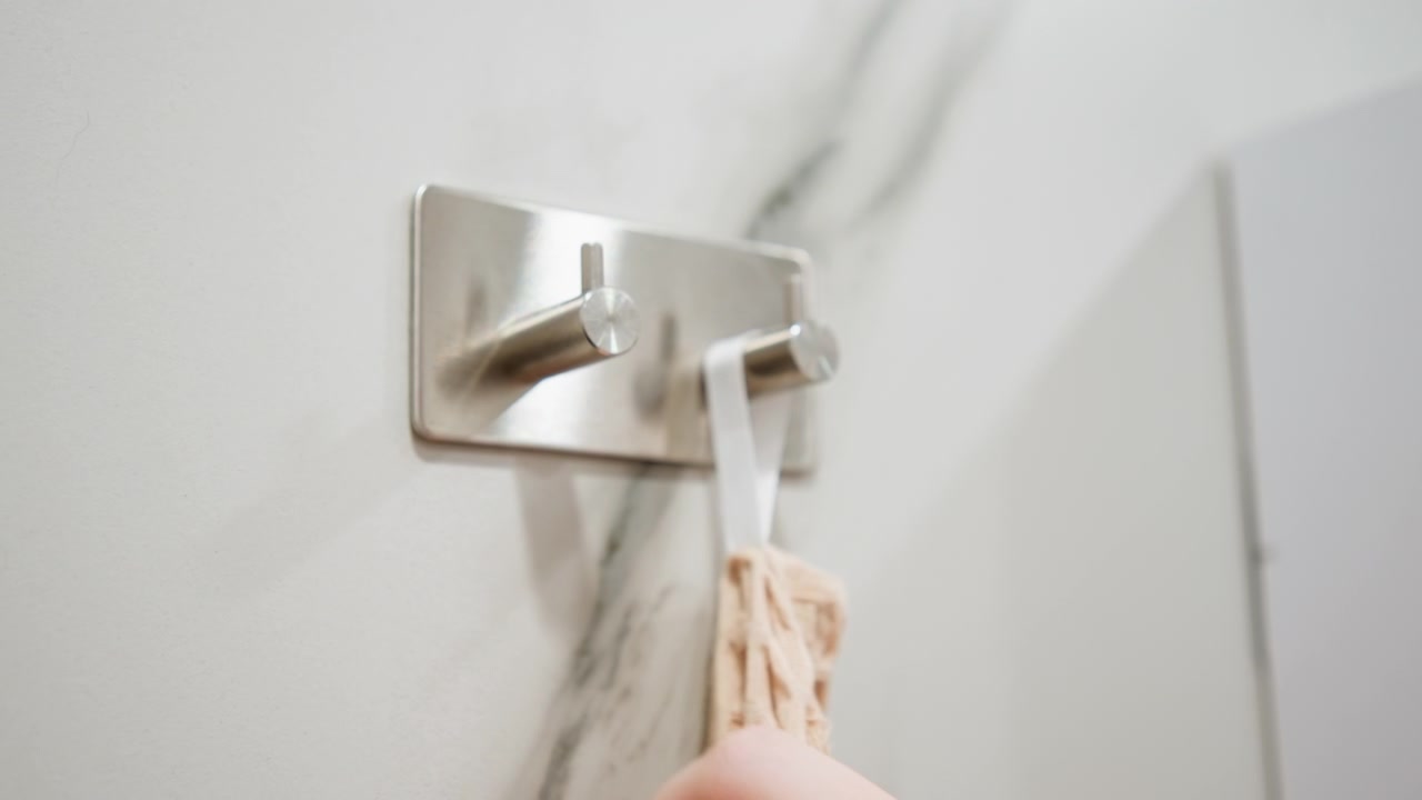 Close-up view of stainless double robe hooks mounted on marble-patterned wall, with hand interaction, hanging towel motion, polished metal finish, modern bathroom detail and practical interior use