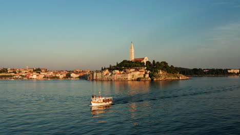 calm scenery of sailing boat with old cityscape of rovinj during sunset at background in istria, croatia