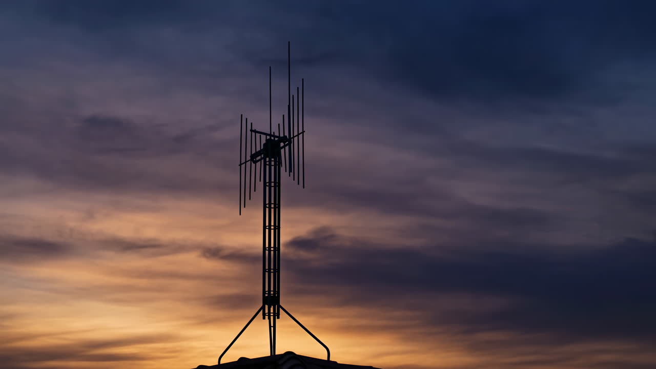 Rooftop Antenna Silhouette At Sunset Against Dramatic Purple And Orange Clouds, Tile Rooftop Outline Visible,