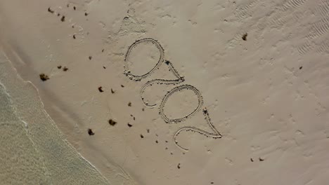 Aerial-camera-looking-straight-down-ascending-showing-Twenty-Twenty-written-in-the-sand-on-a-beach