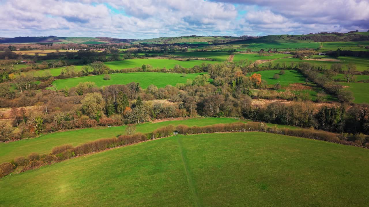 Wide aerial drone view of rolling farmland fields and hedgerows with layered countryside landscape in Wiltshire, United Kingdom on a bright day