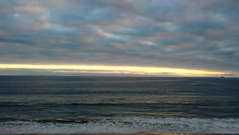 olas del océano rodando en la playa con tonos de puesta de sol en el horizonte